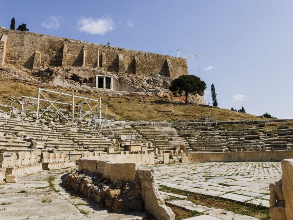 Ancient stone amphitheater ruins under a clear blue sky, with no visible Dionysus kantharos or other figures
