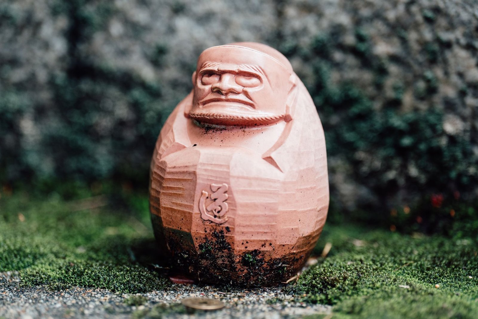 Hand-carved wooden kappa figurine with detailed face sitting outdoors on grass
