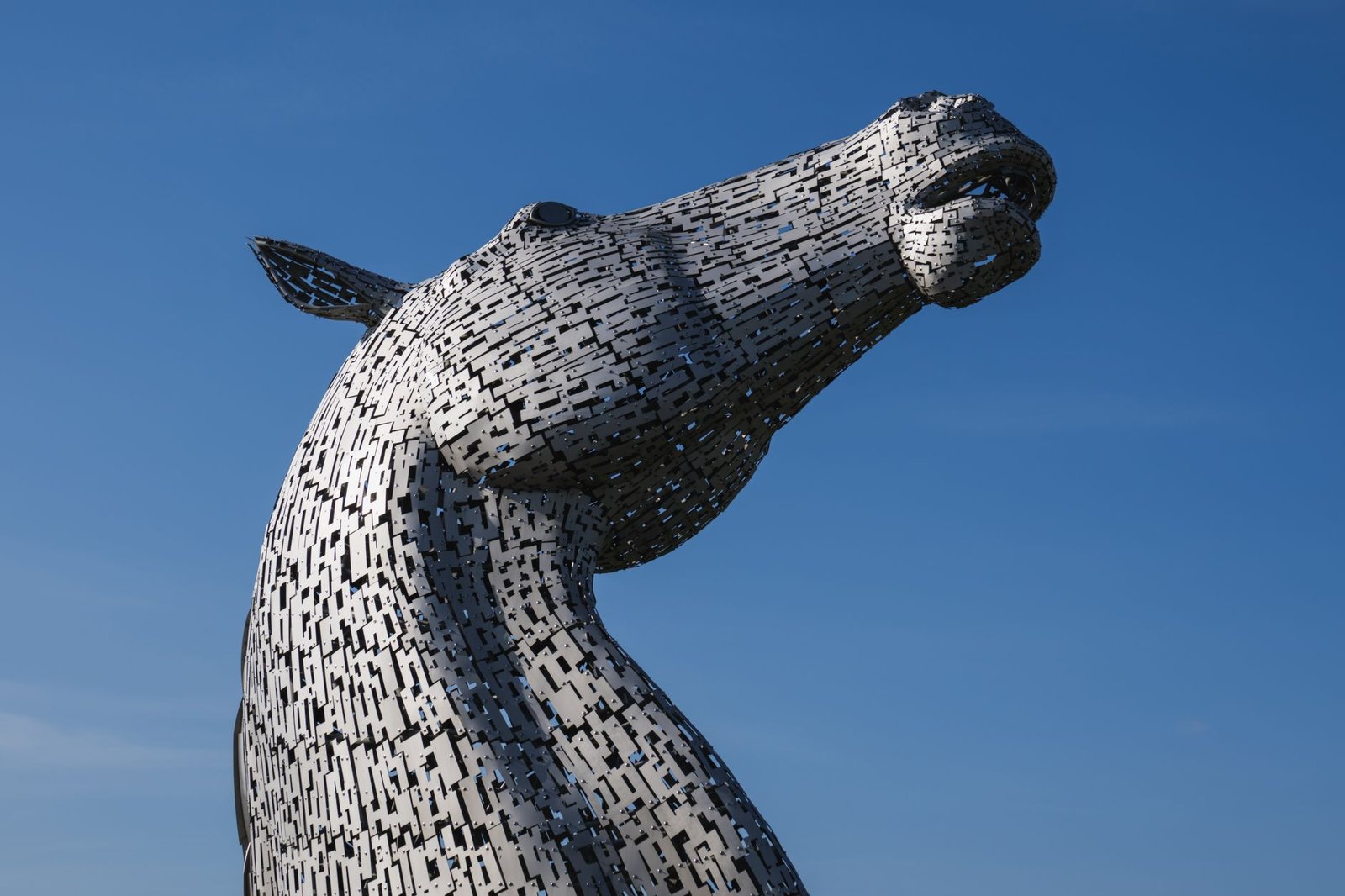 Close-up of a large metal horse head sculpture against a clear blue sky, evoking the Scottish kelpie myth