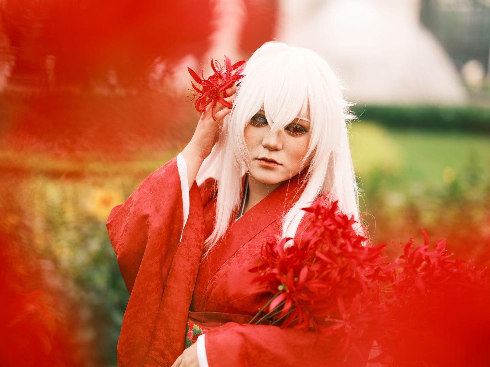 Woman in white wig and red kimono holding red flowers, portraying Konohanasakuya-Hime outdoors