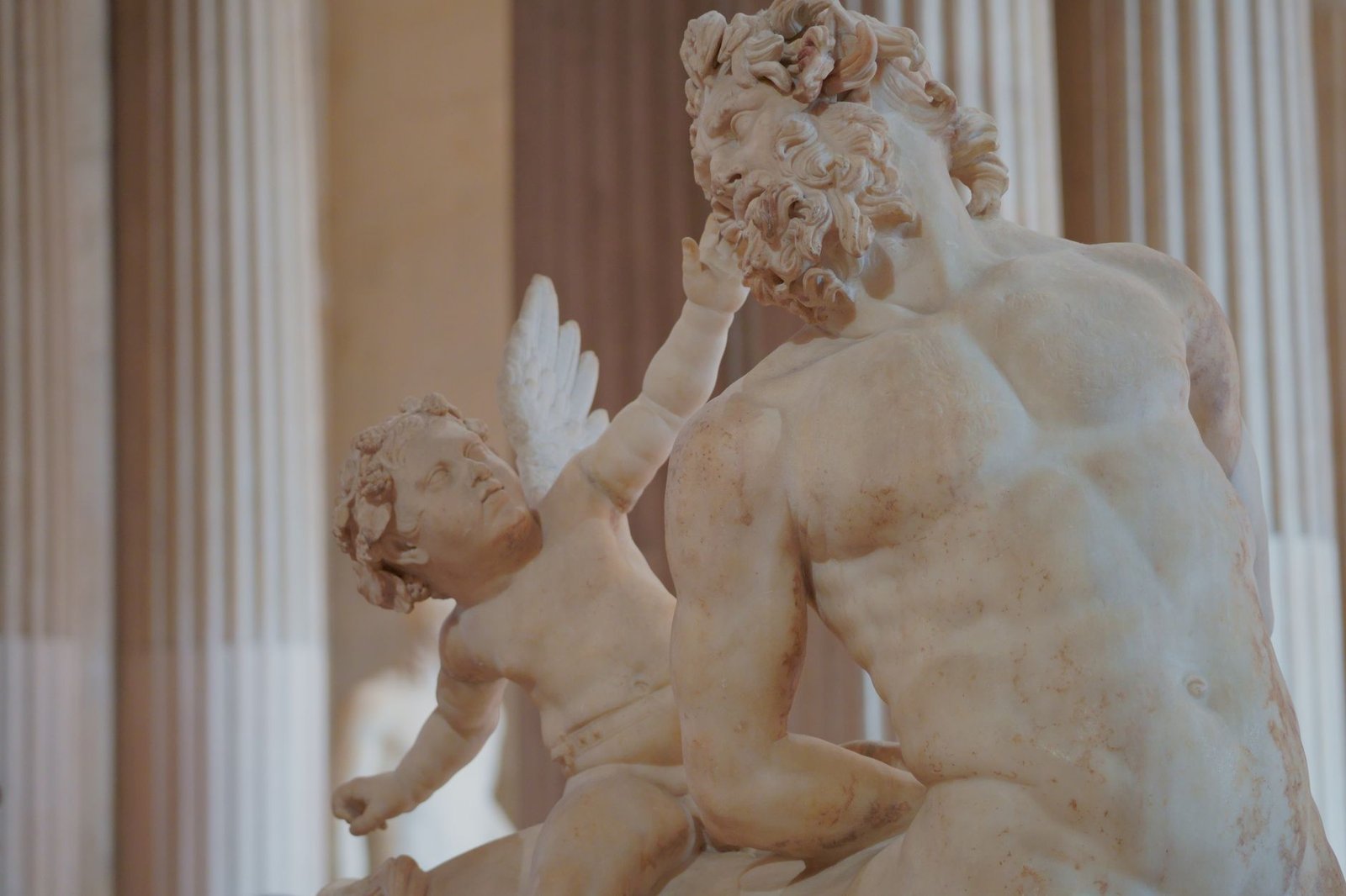 Marble statue of a muscular man and a cherub in a classical museum setting, representing Ladon Greek mythology