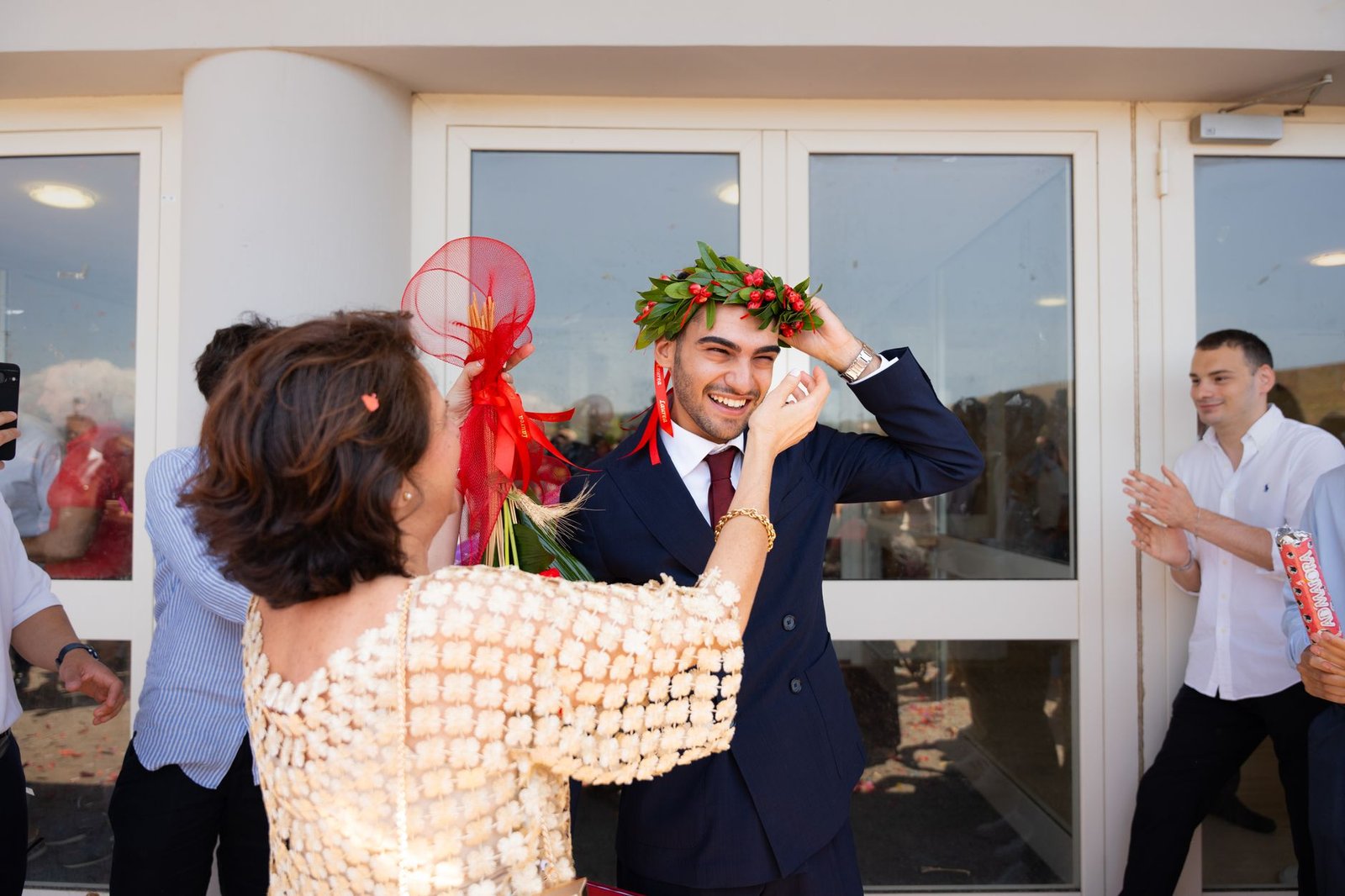 Young man in graduation attire wearing a laurel wreath amid falling confetti