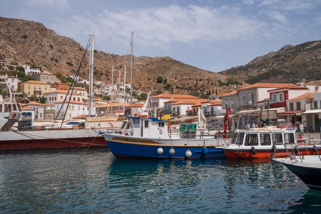 Boats docked in a coastal harbor with hillside buildings in the background, evoking the Lernaean Hydra setting