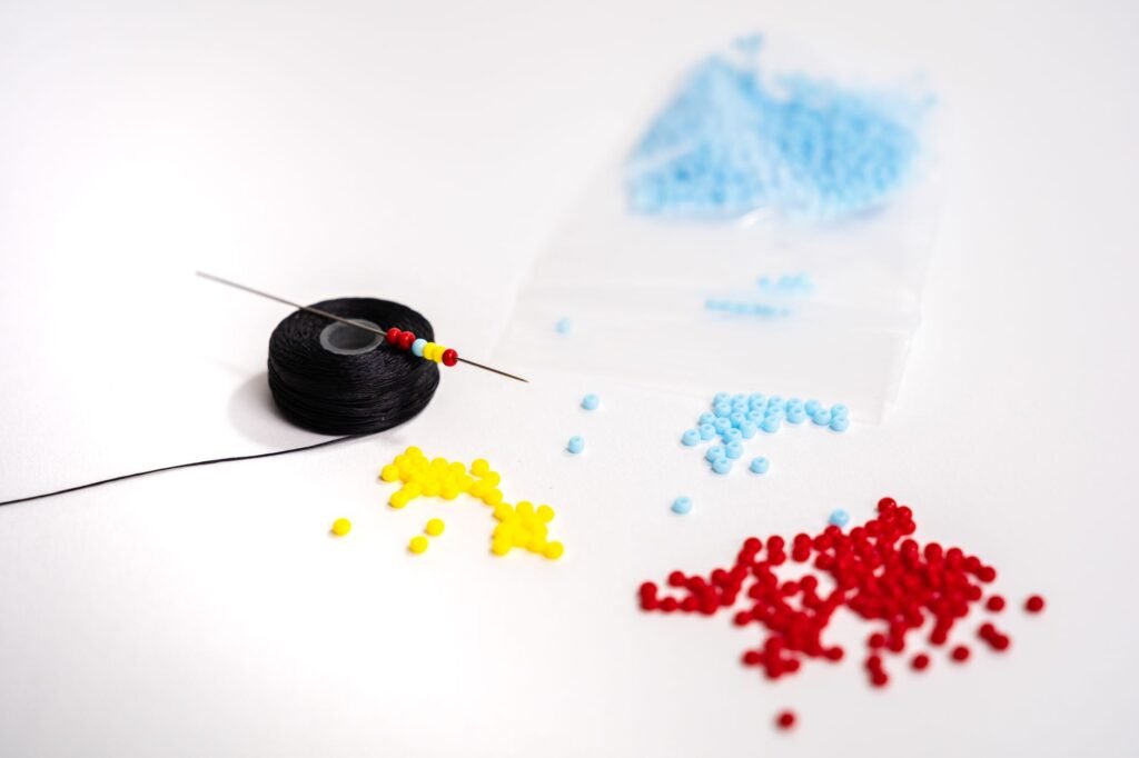 Colorful magatama beads, beading thread, and a needle arranged on a white surface