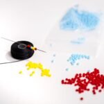 Colorful magatama beads, beading thread, and a needle arranged on a white surface
