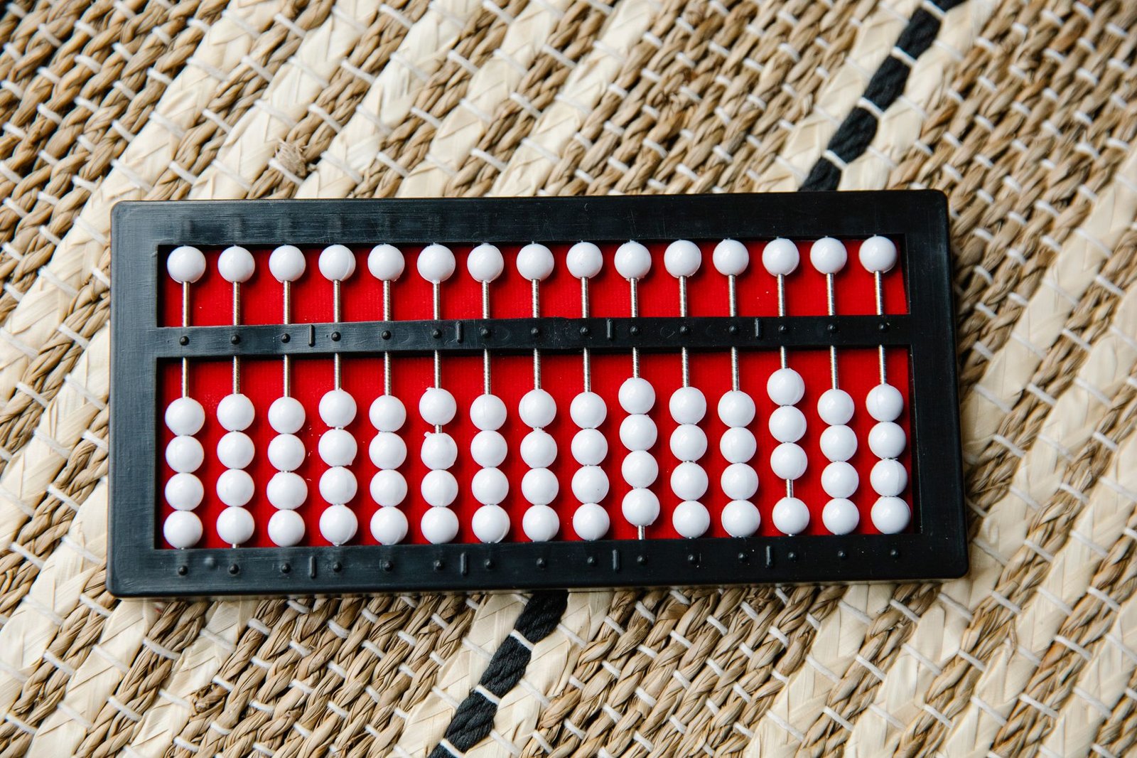 Black and red abacus with white beads resting on a woven mat background