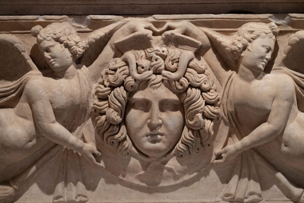Ancient stone relief of Medusa’s head flanked by two winged figures
