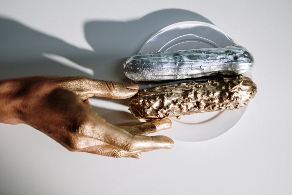 Hand with gold paint reaching toward two textured stones on a white surface