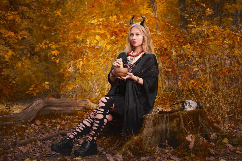Young woman in a Halloween costume sitting in an autumn forest and holding a pumpkin