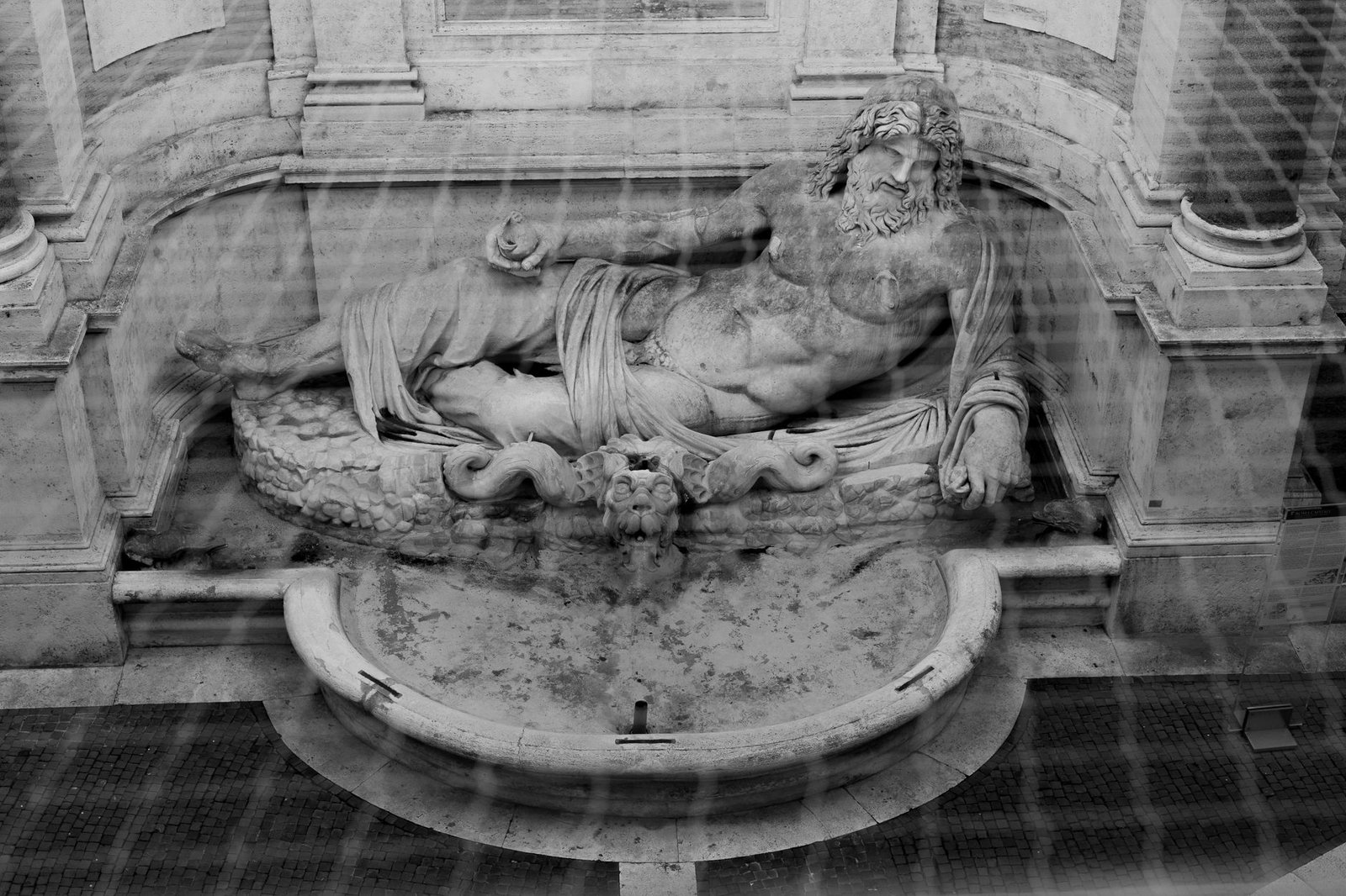 Reclining stone statue of Neptune, Roman sea god, in an architectural setting in black and white