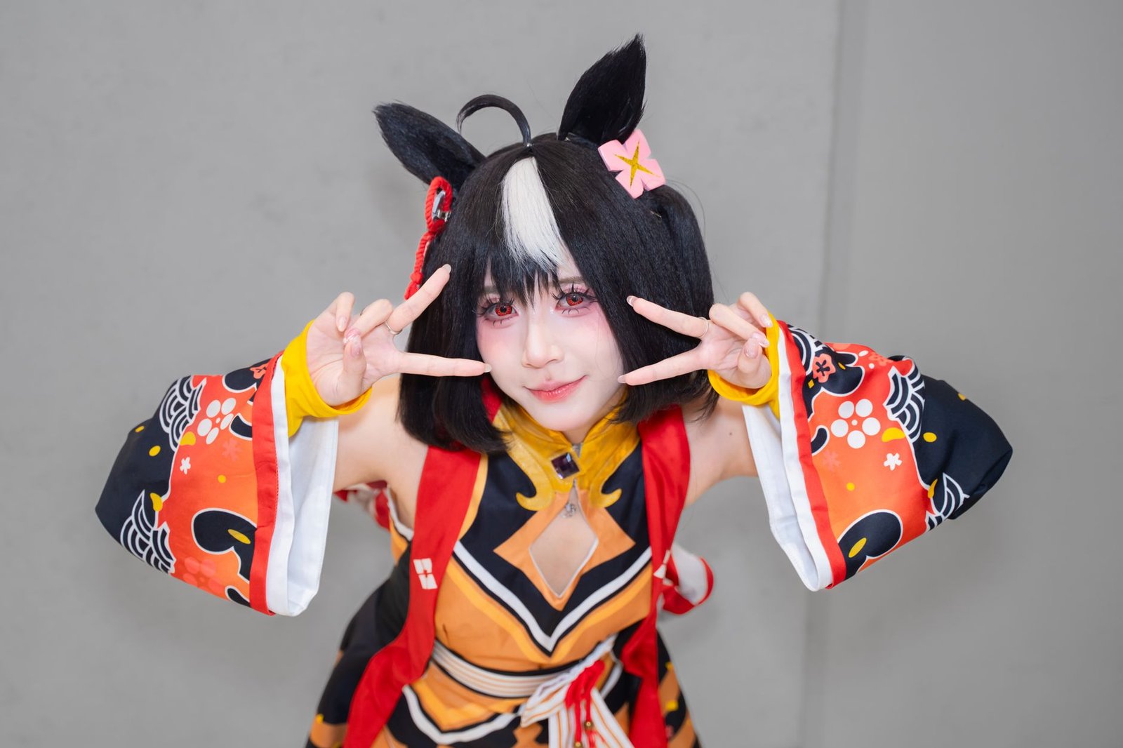 Cosplayer with black and white hair, cat ears, and orange-black outfit as Ninigi no Mikoto from Japanese mythology