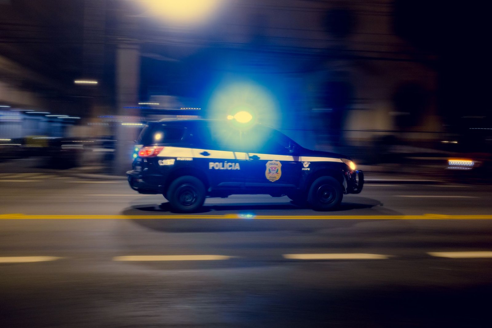 Police car with flashing lights speeding down a city street at night