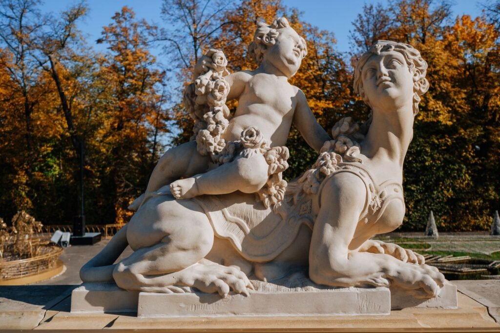 Marble cherub beside a sphinx statue in an autumn park, with fallen leaves and trees in the background