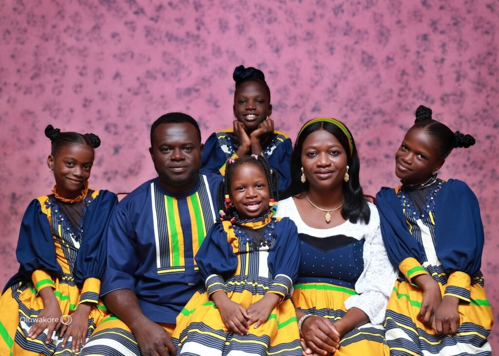 Smiling African family in colorful traditional attire posed against a pink patterned background