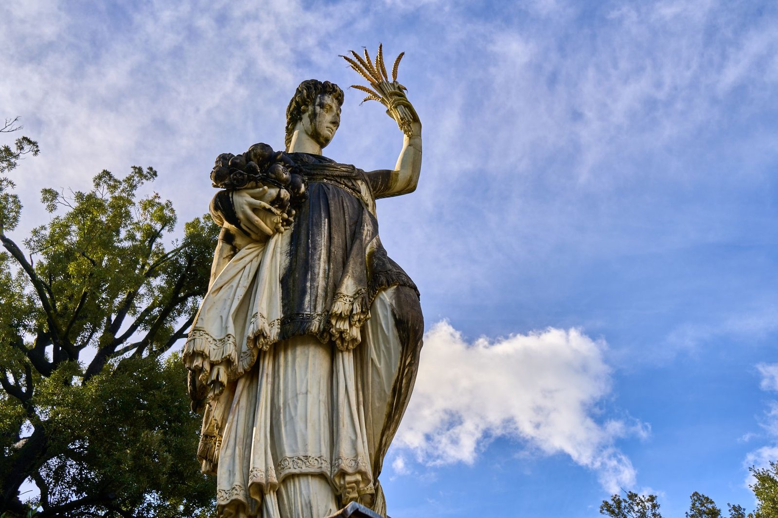 Statue of a woman holding a bouquet against a blue sky with clouds