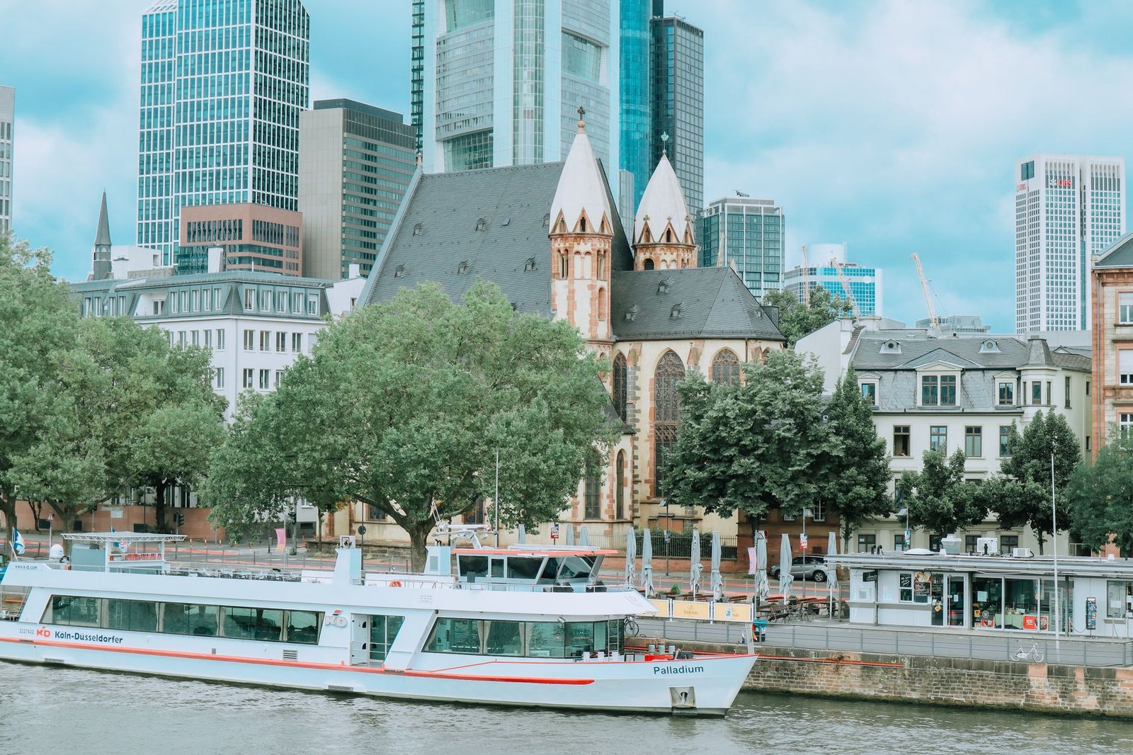 River cruise boat on a city river passing historic and modern buildings under a clear sky