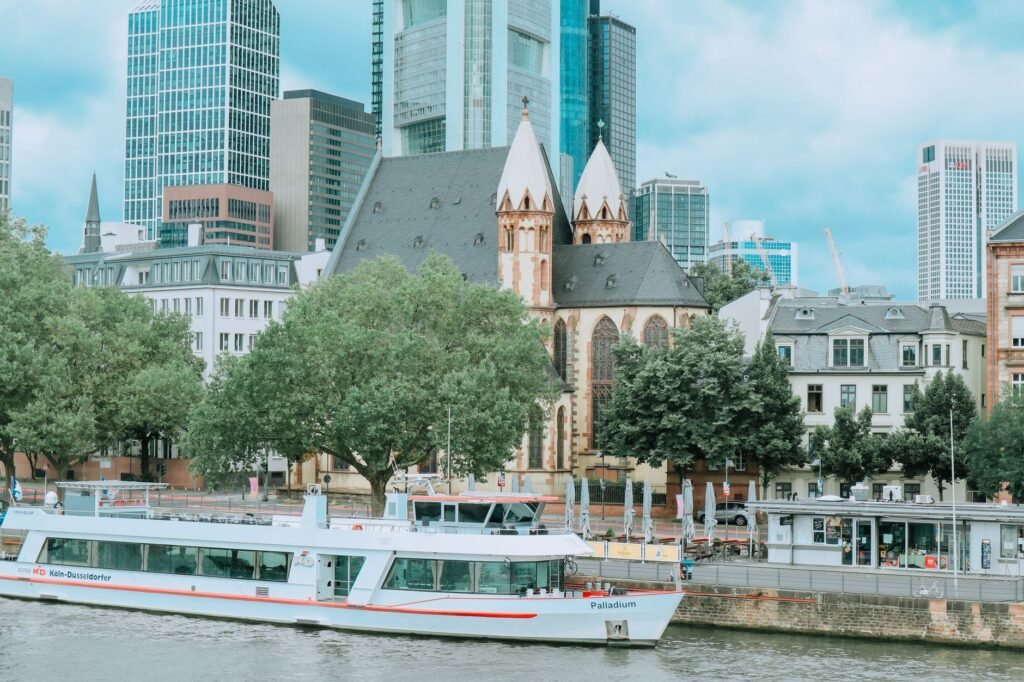 Frankfurt cityscape with a historic church, modern skyscrapers, and a river cruise boat on the river