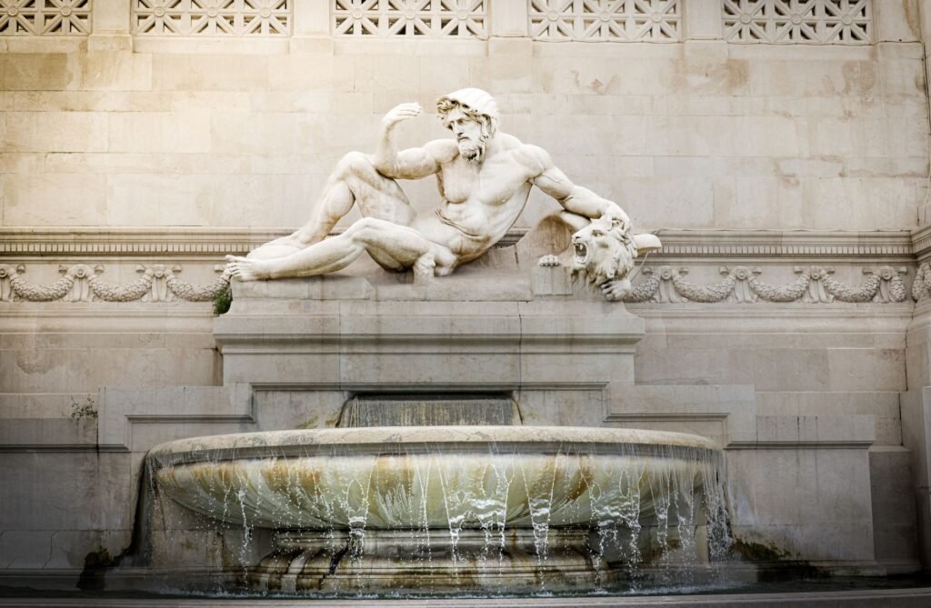 Classical marble statue of a reclining male figure above an ornate stone fountain in a Phaethon myth scene
