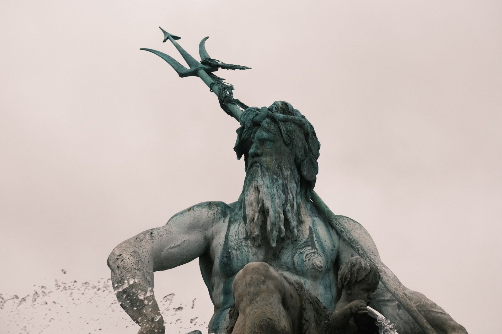 Statue of Poseidon holding a trident against a cloudy sky