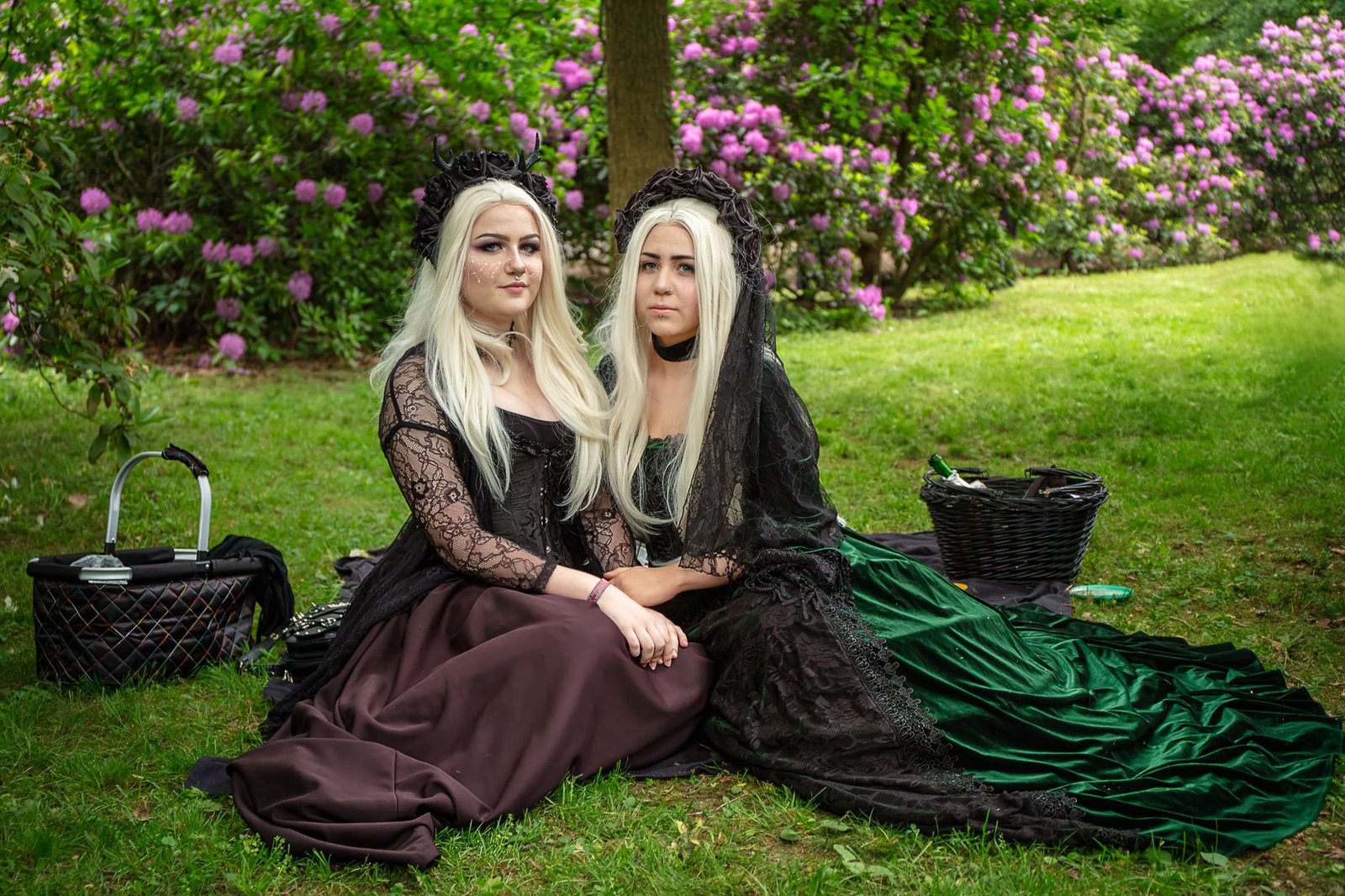 Two women in elegant vintage dresses sit on grass in a flower garden, evoking Rhiannon from Welsh mythology