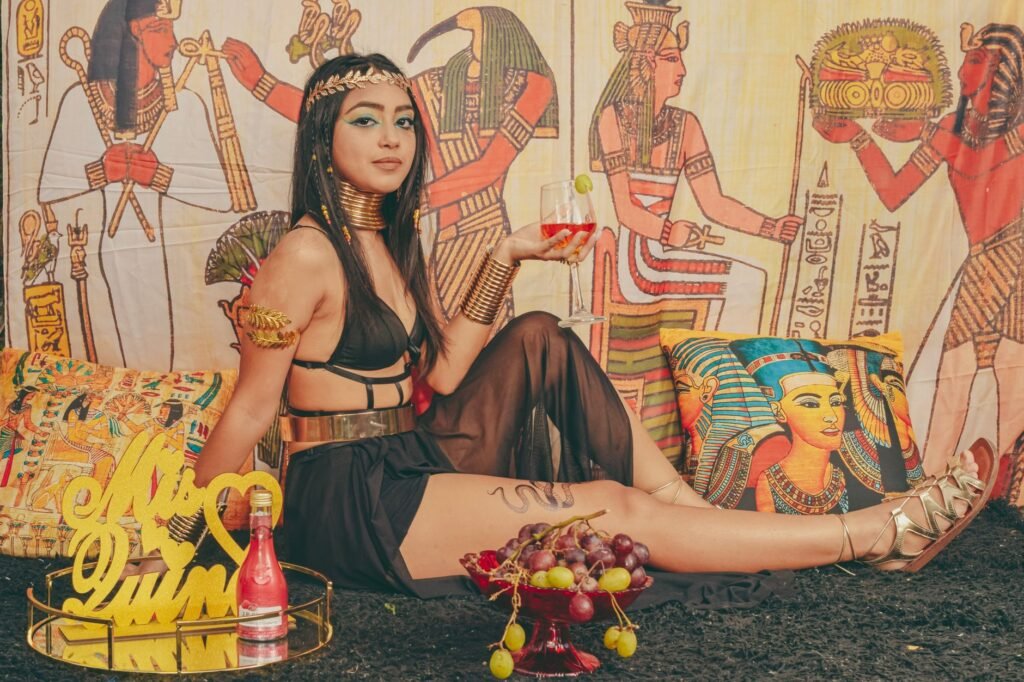 Woman in ancient Egyptian dress posing before wall art of the goddess Renenutet and harvest symbols