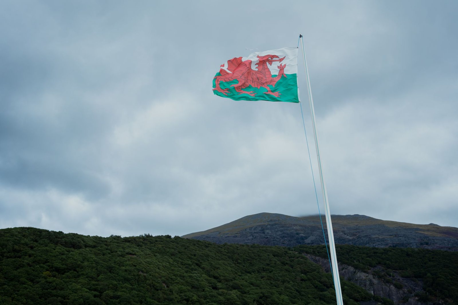 Welsh flag flying on a pole against a cloudy sky and mountainous landscape