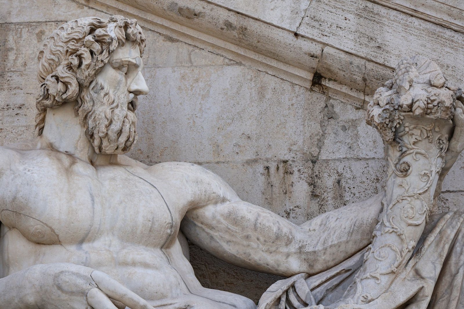Close-up of a marble statue of a muscular bearded man holding a decorative horn, representing the Roman god Robigus