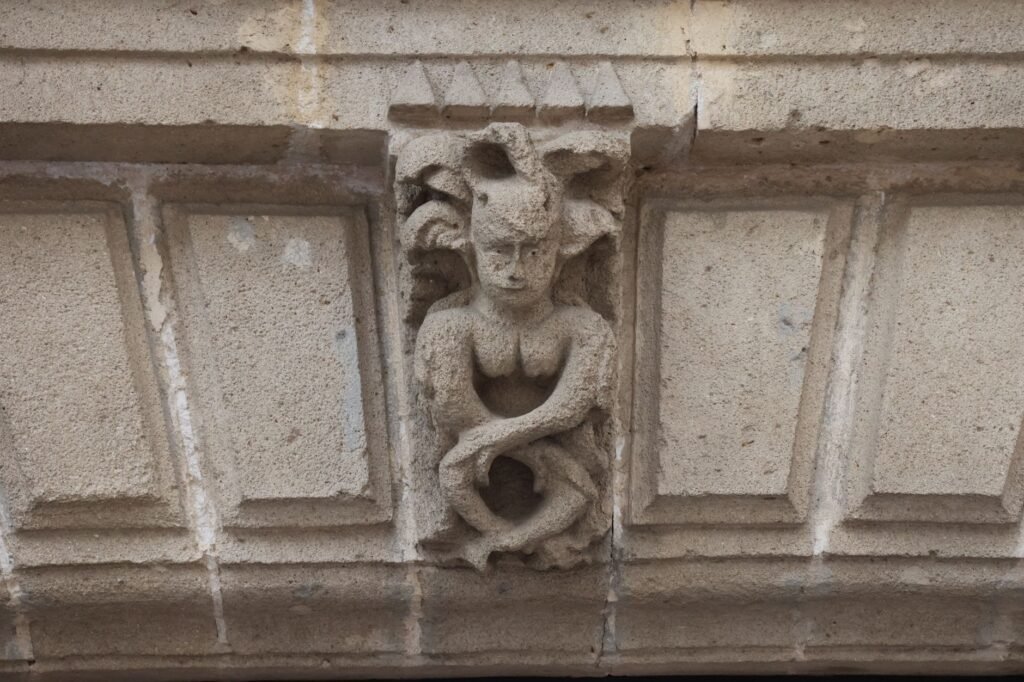Close-up of a stone gargoyle sculpture on a historic building facade with carved mythical features