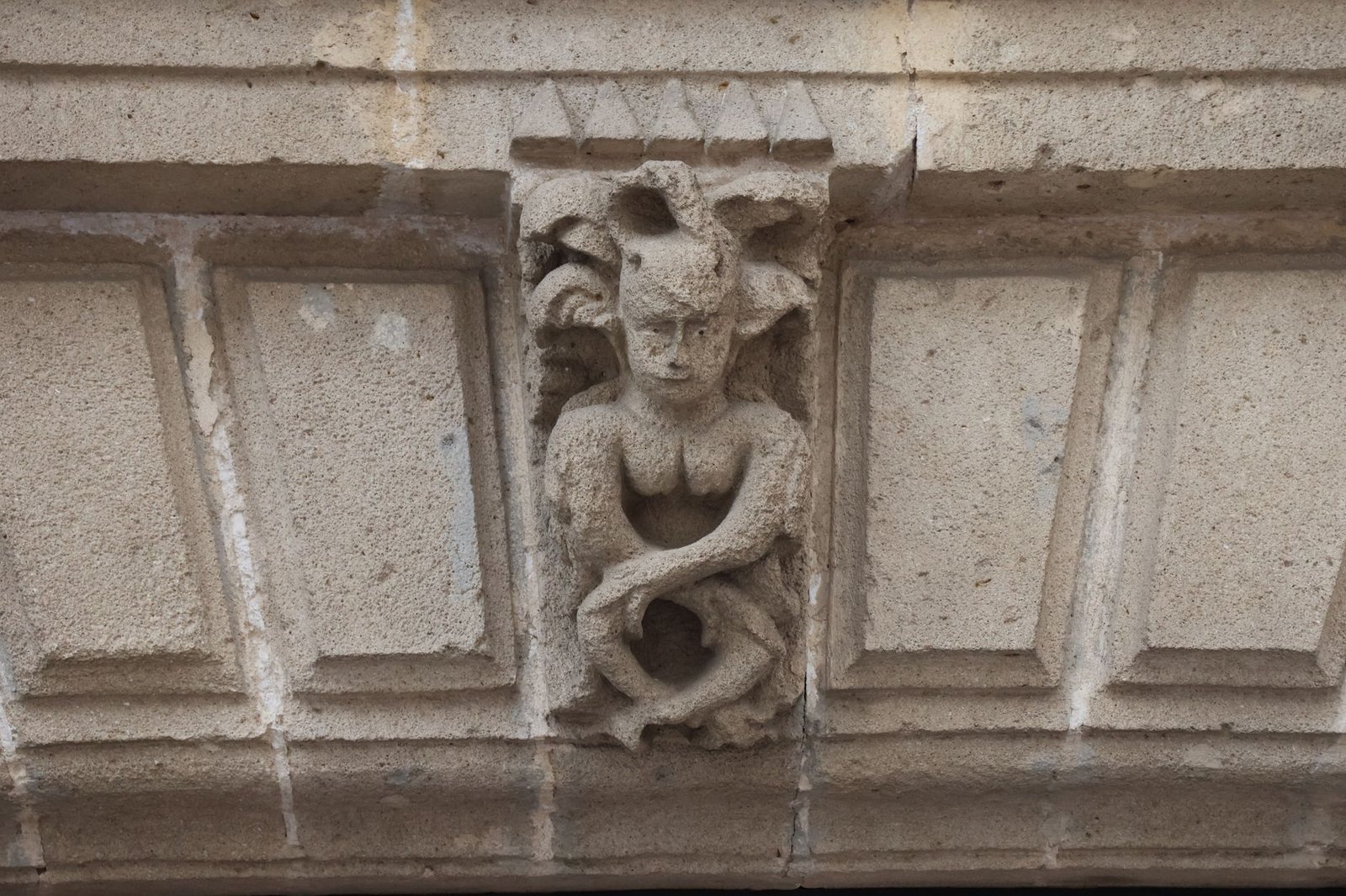 Close-up of a stone facade carving showing a mythical creature on a building exterior