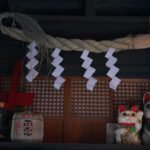 Shimenawa rope at a Japanese shrine with maneki-neko lucky cat figurines and decorative sacred ornaments