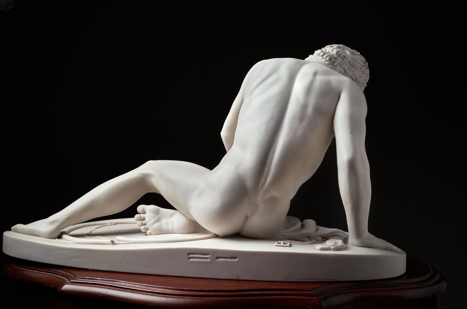 Marble sculpture of Sisyphus seated nude from behind on a wooden base, depicting his punishment in Greek mythology