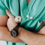 Healthcare professional in green scrubs with stethoscope, arms crossed, symbolizing the Staff of Asclepius theme