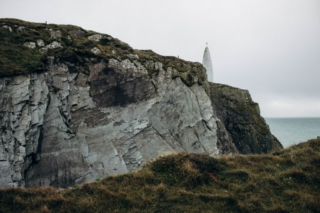 Cliffside lighthouse overlooking the ocean under cloudy skies, a modern landmark beside the legendary Lia Fáil Stone theme