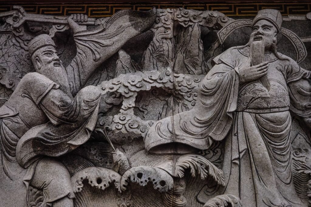 Intricate stone carving of ancient Chinese figures in traditional attire, standing in a carved relief scene