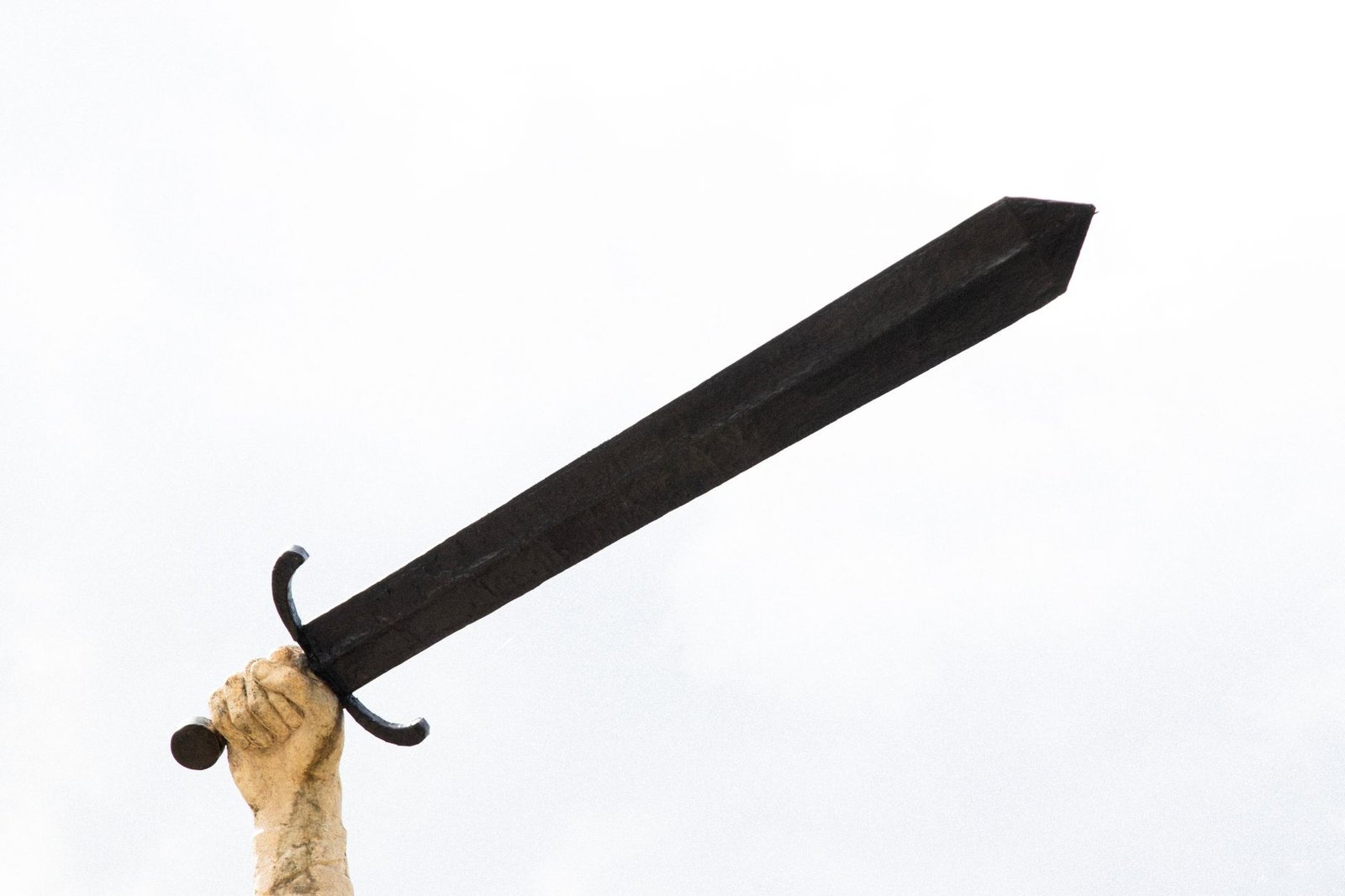 Hand holding a large black sword against a white background