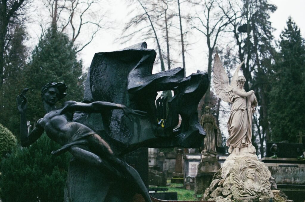 Abstract bronze sculpture beside a classical stone statue in an outdoor garden setting