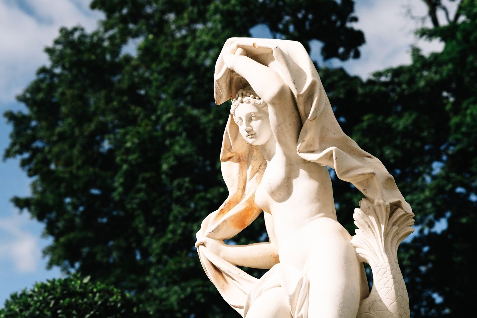 Classical marble statue of a draped woman with trees and blue sky behind her, evoking Pandora from Greek myth