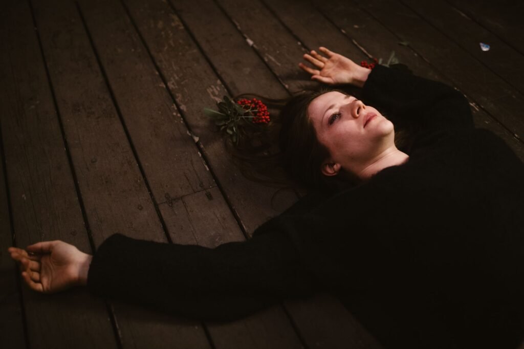 Woman lying on a wooden floor beside a red rose, evoking Deirdre of the Sorrows from Irish mythology