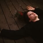 Woman lying on a wooden floor beside a red rose, evoking Deirdre of the Sorrows in Irish mythology