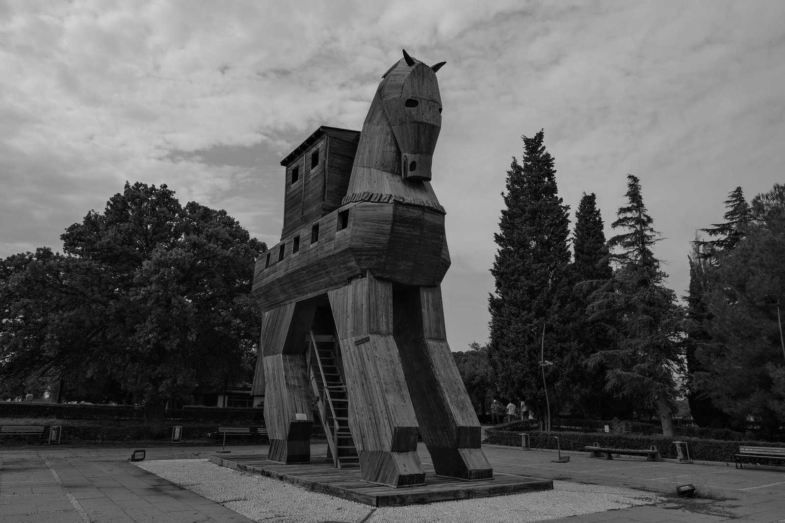 Black and white photo of a wooden Trojan horse sculpture in an outdoor park setting