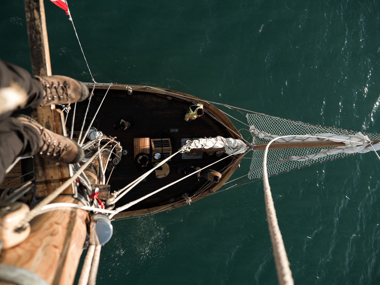 Person standing on a sailboat mast, looking down at the boat and ocean from above, evoking The Voyage of Bran