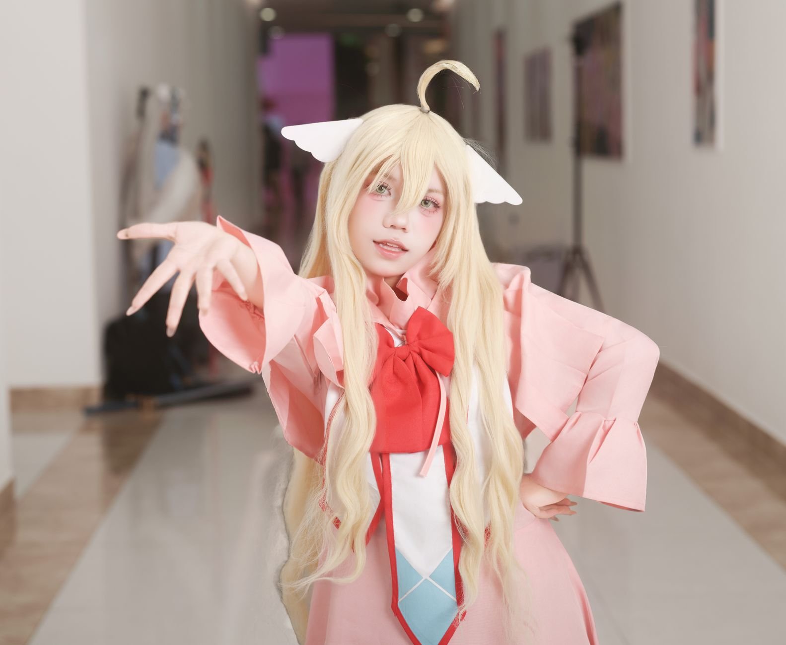 Cosplayer with long blonde hair in a pink outfit posing in a hallway as Toyotama-Hime, Japanese sea princess