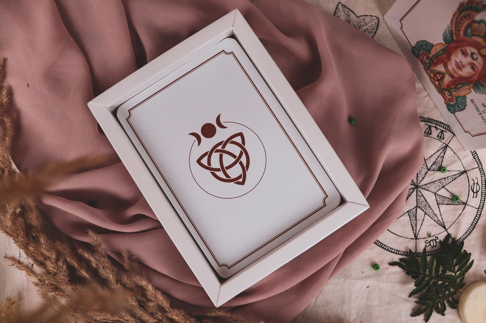 White tarot card with mystical symbols, including a triquetra symbol, resting on pink fabric background