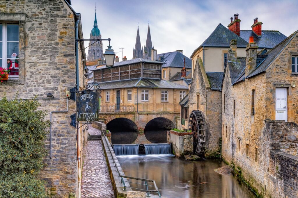 Historic European town with stone buildings and a watermill beside a river, evoking a Celtic triskele symbol legacy