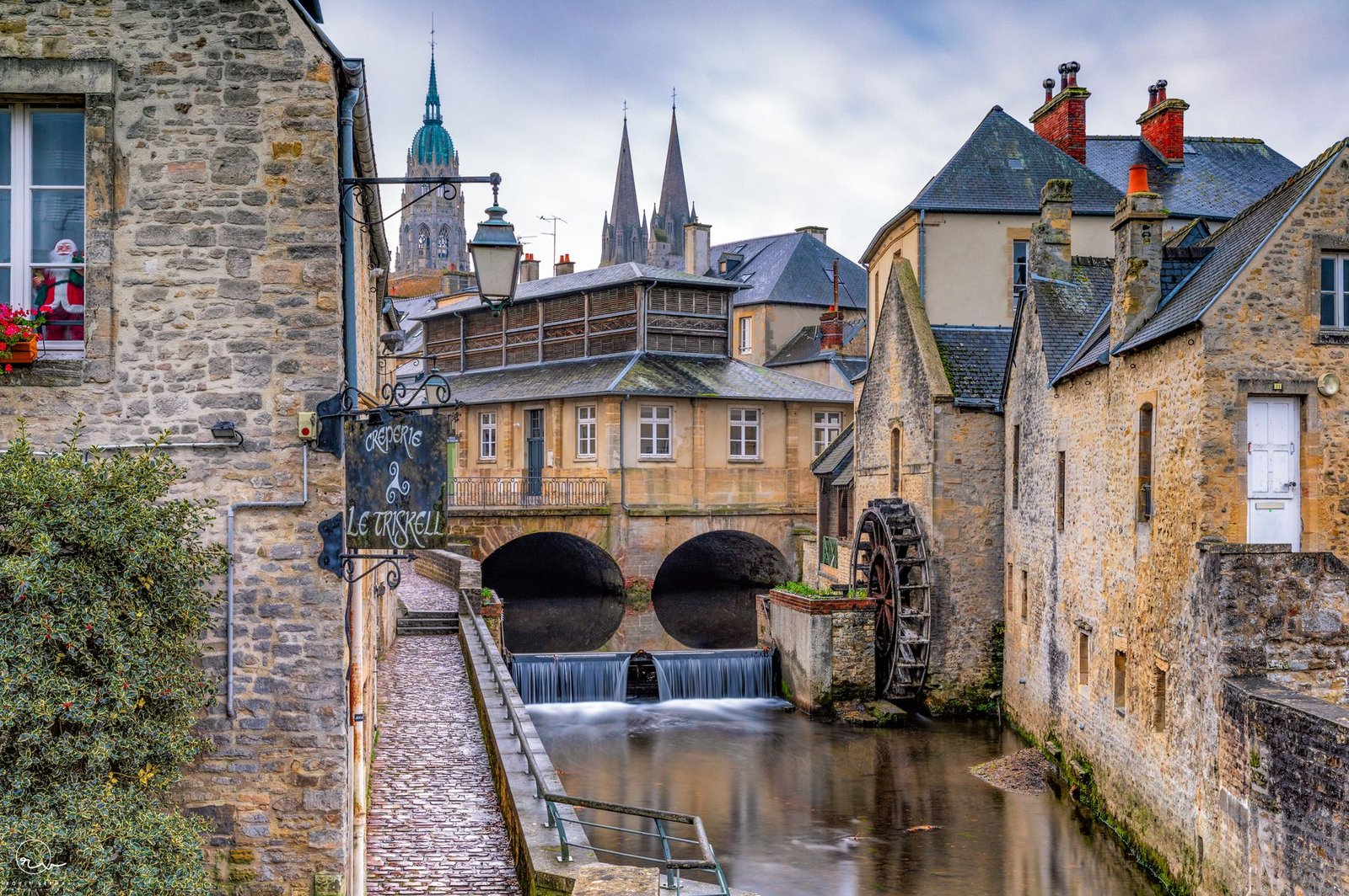 Historic European town with stone buildings and a watermill beside a river, evoking a Celtic triskele symbol legacy