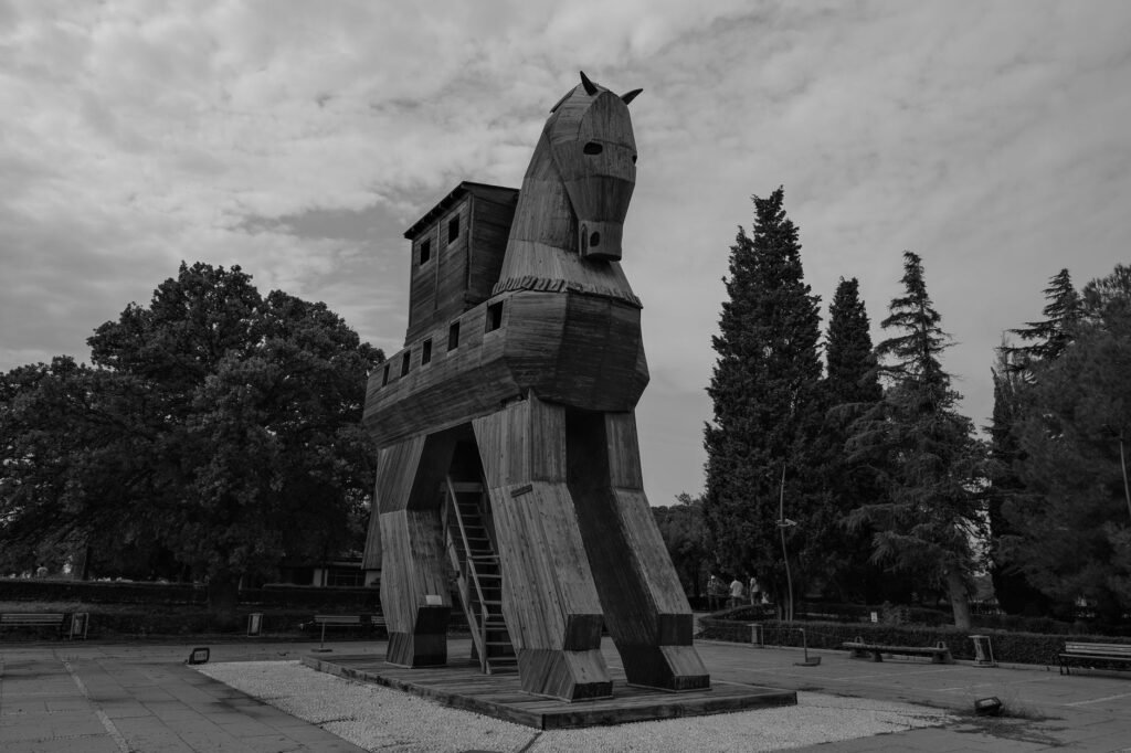 Black and white photo of a wooden Trojan horse statue in an outdoor park setting.
