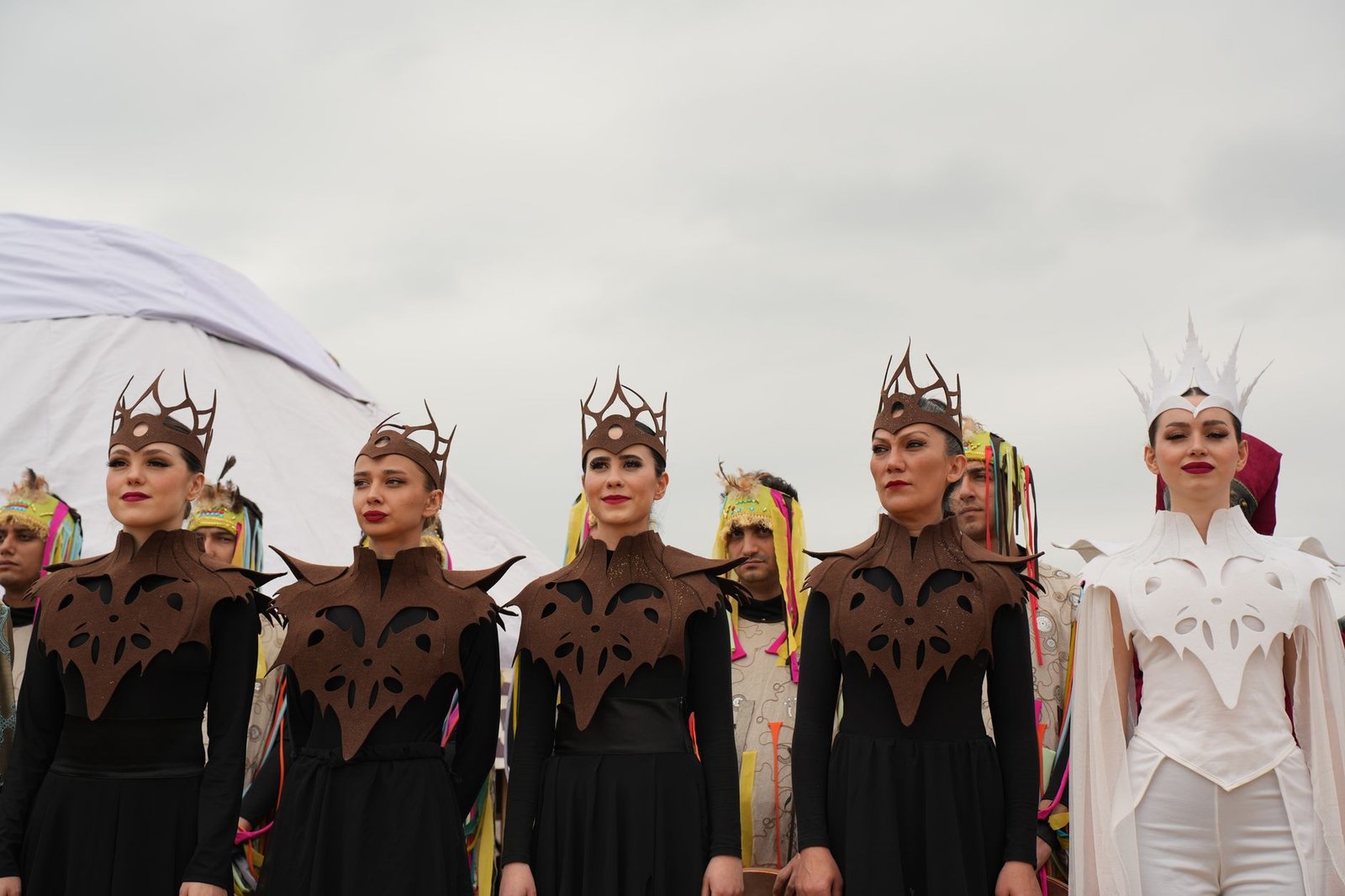 Performers in elaborate Tuatha Dé Danann and Fomorians costumes stand outdoors beneath a cloudy sky