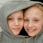 Two smiling children sharing a gray hoodie, facing opposite directions like Janus with two faces