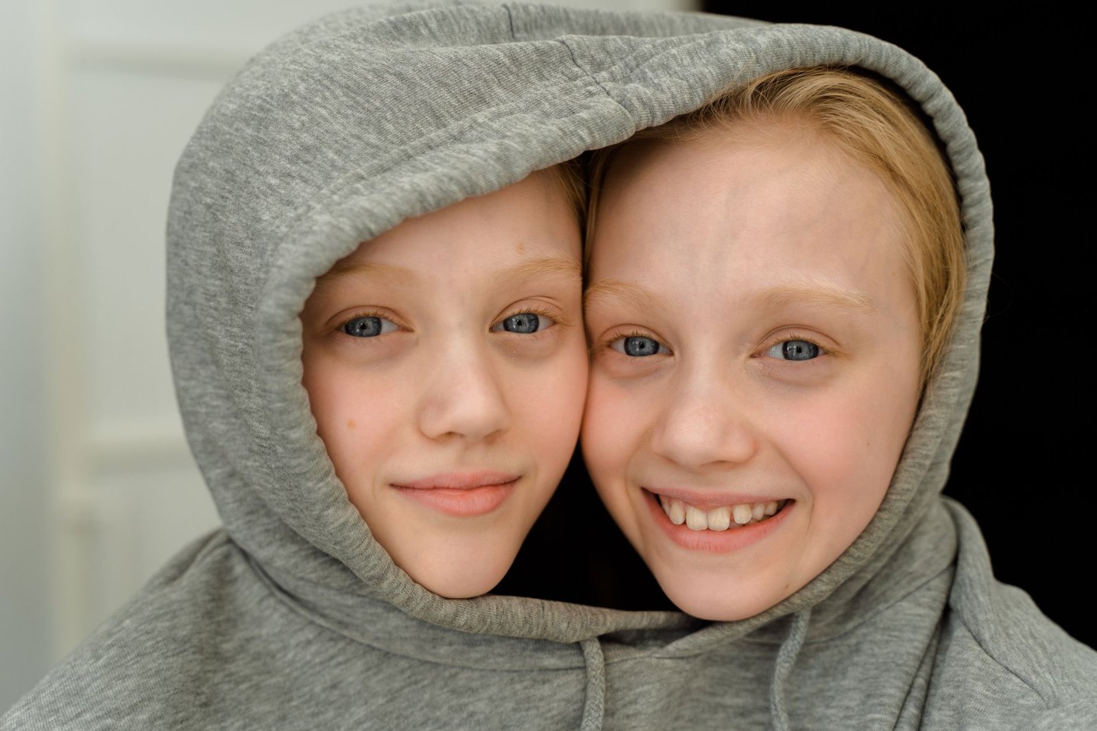 Two smiling children sharing a gray hoodie, facing opposite directions like Janus with two faces