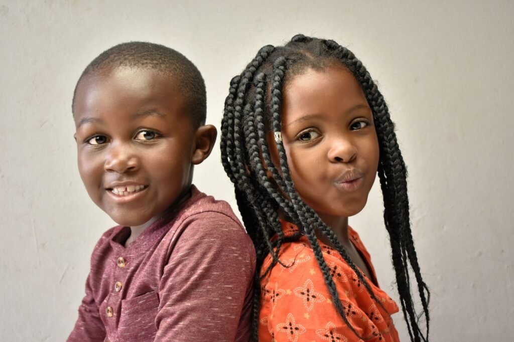 Smiling African American siblings posing back to back against a plain background